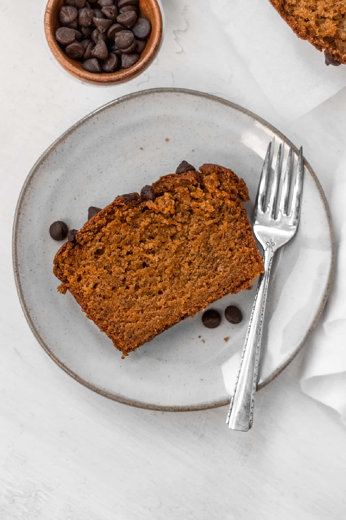 Overhead view of one slice of vegan pumpkin bread on a plate with a fork on the side. 