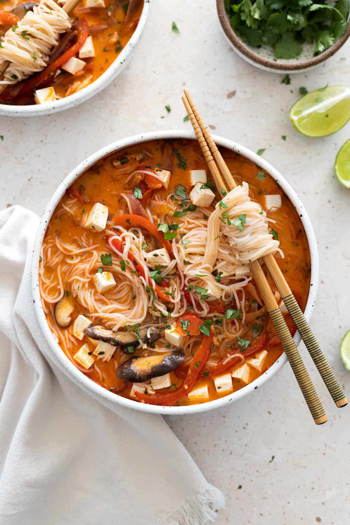 Overhead view of Thai red curry noodle soup in a white bowl with chopsticks on the side. 