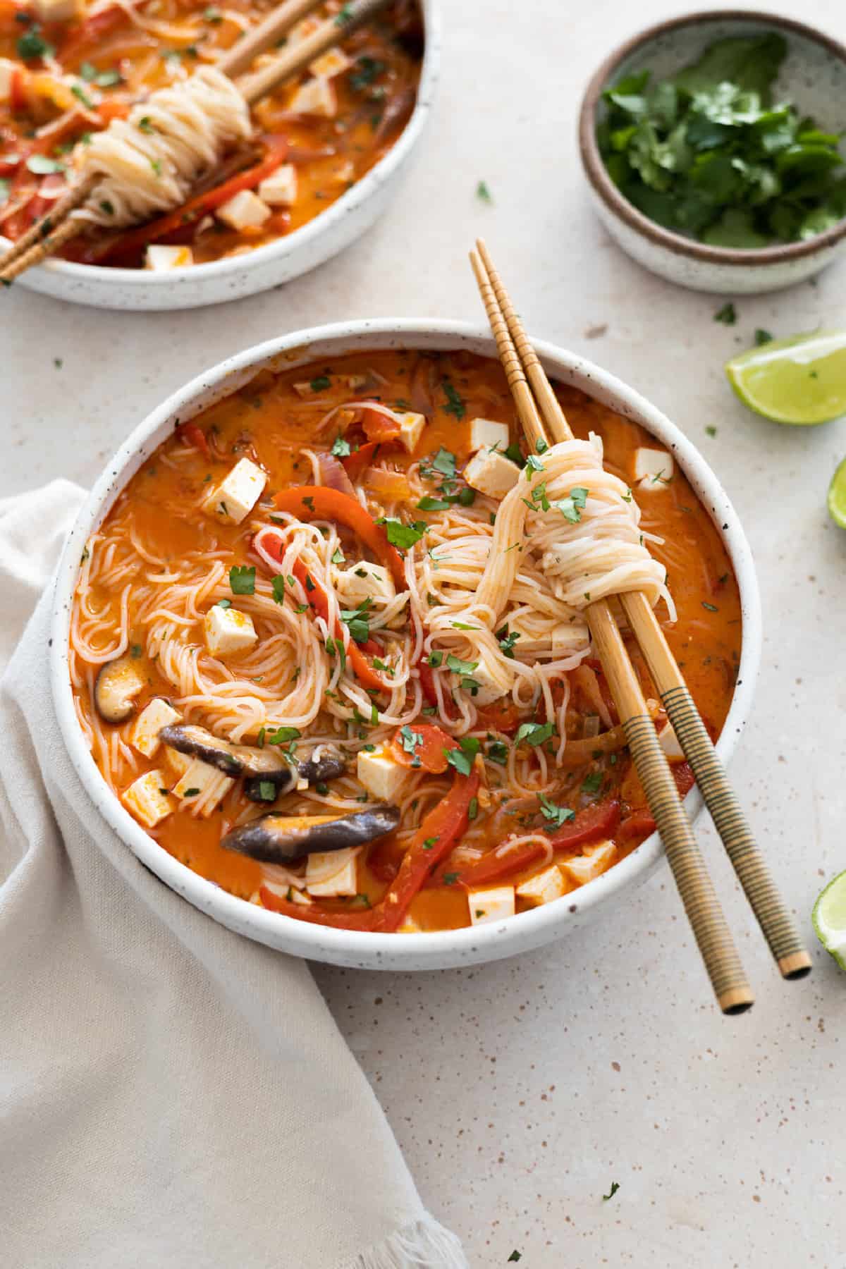 Front view of Thai red curry noodle soup in a white bowl with chopsticks on top. 