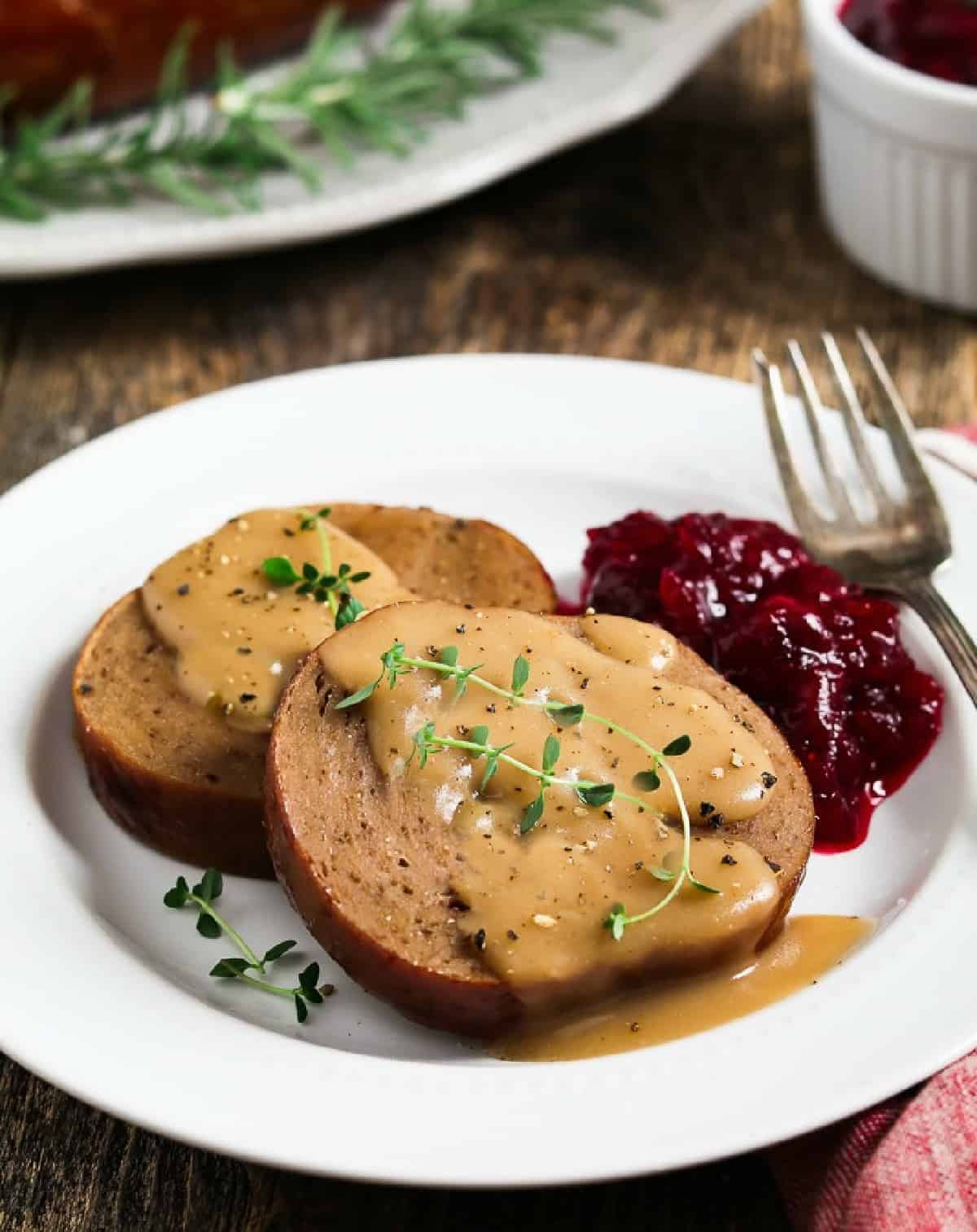 Two slices of vegan holiday roast on a  white plate with gravy on top.