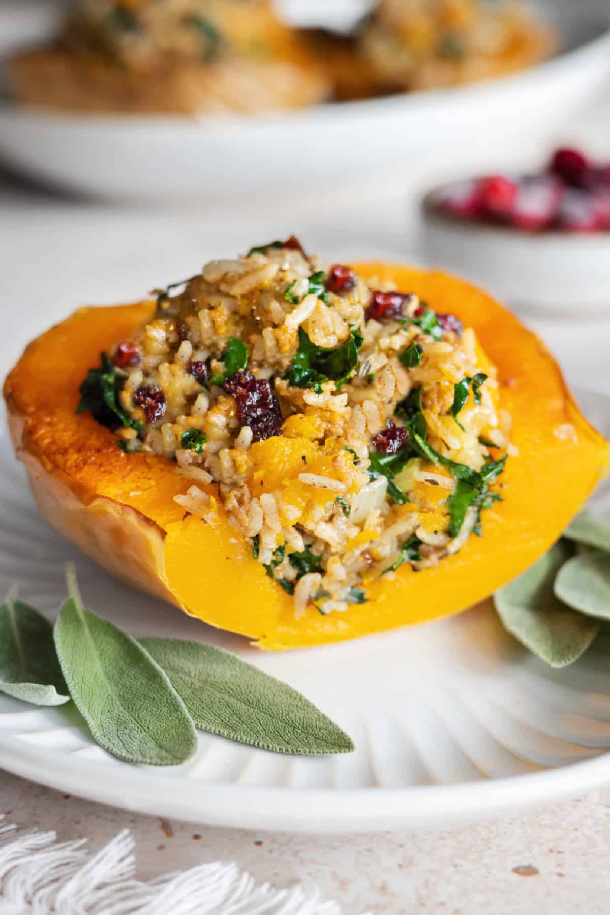 One slice of stuffed butternut squash on a white plate with sage leaves on the side.