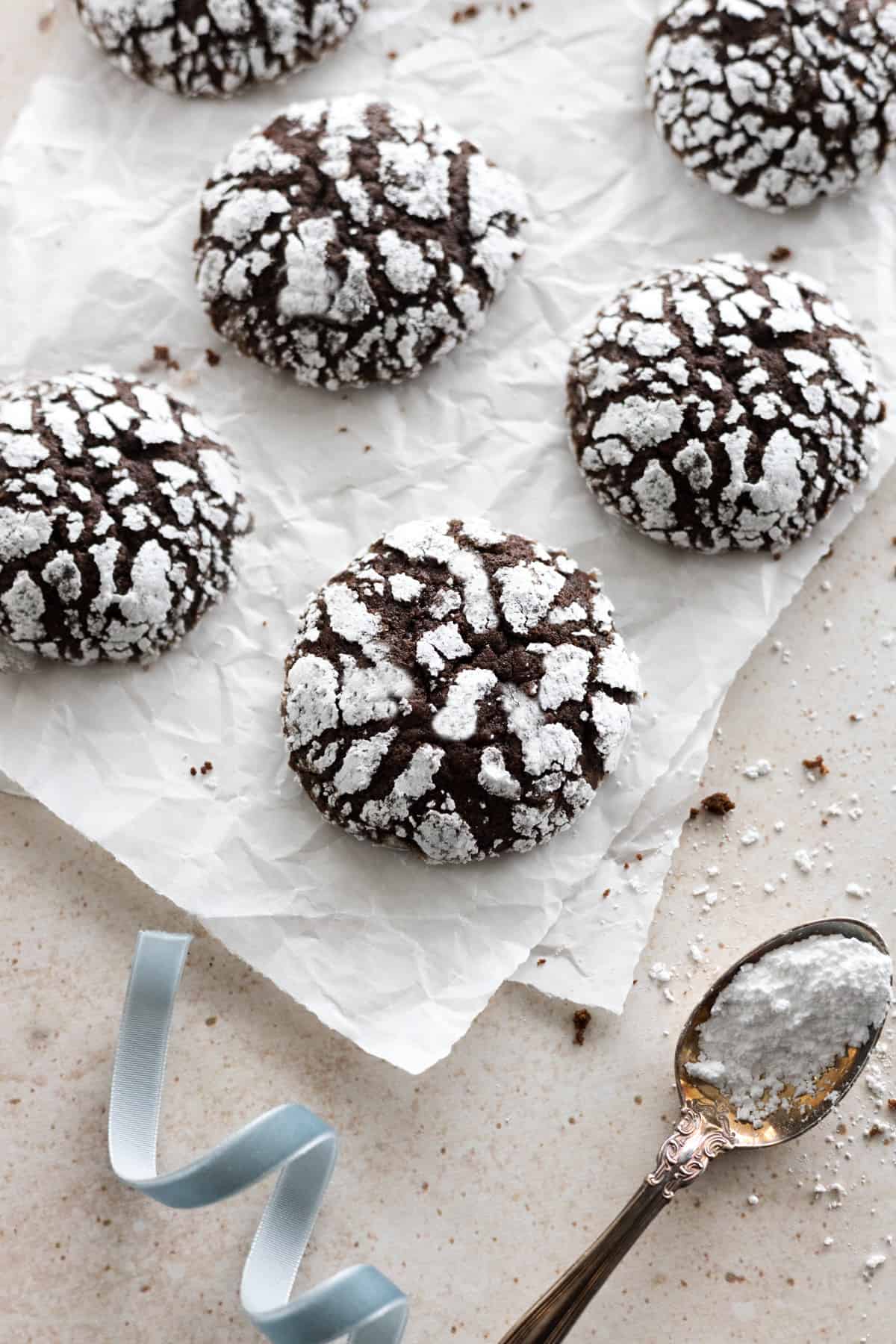 Fully baked vegan chocolate crinkle cookies on white parchment paper. 