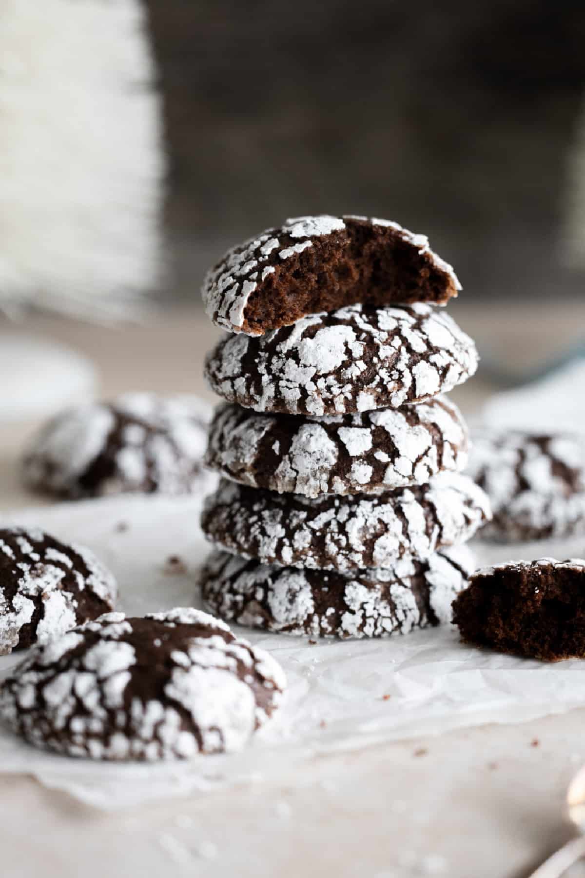 Five vegan chocolate crinkle cookies stacked on parchment paper with broken cookies on the side. 