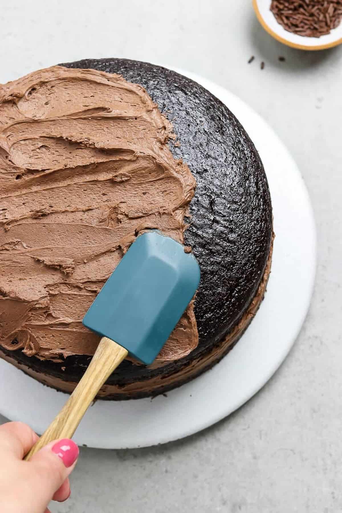 Frosting a vegan chocolate cake with a rubber spatula. 