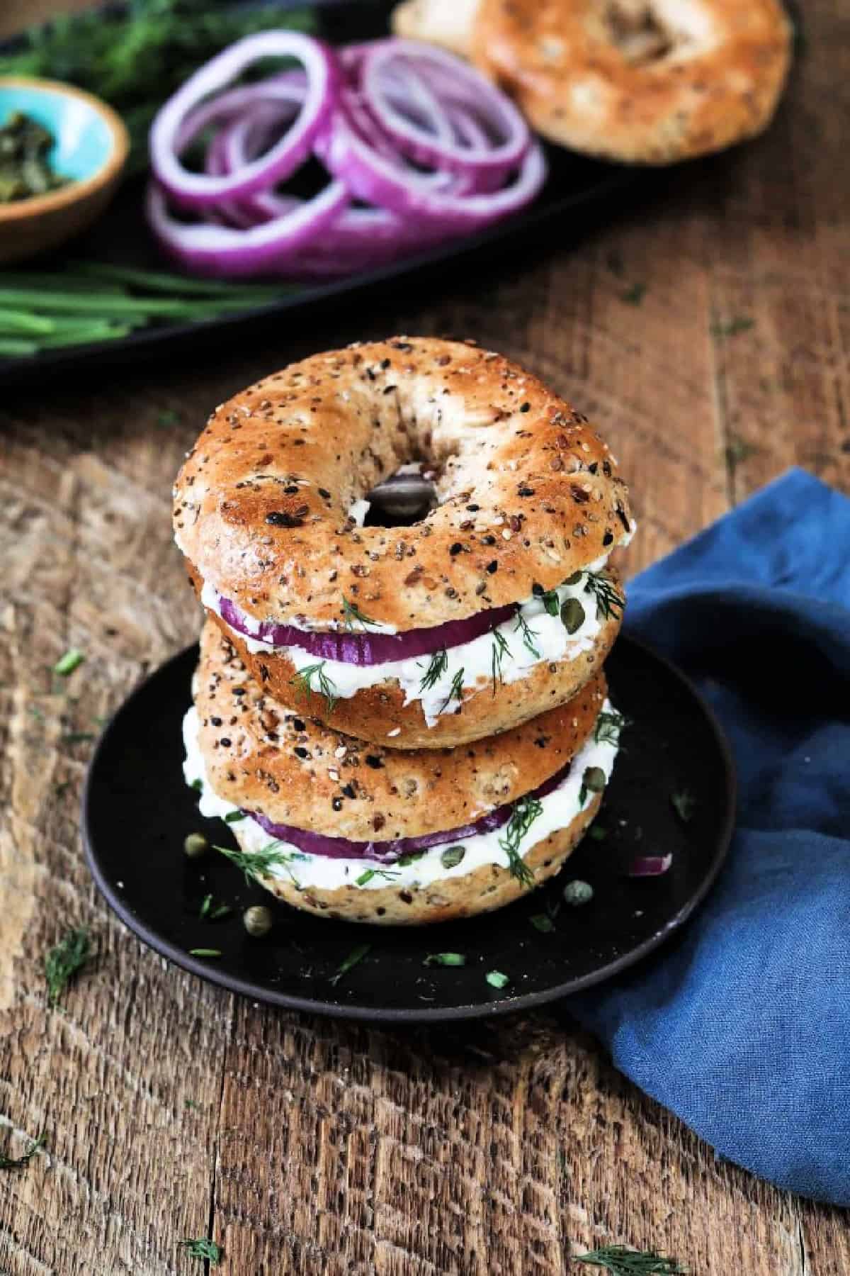 Two bagels with vegan cream cheese stacked together on a black plate. 