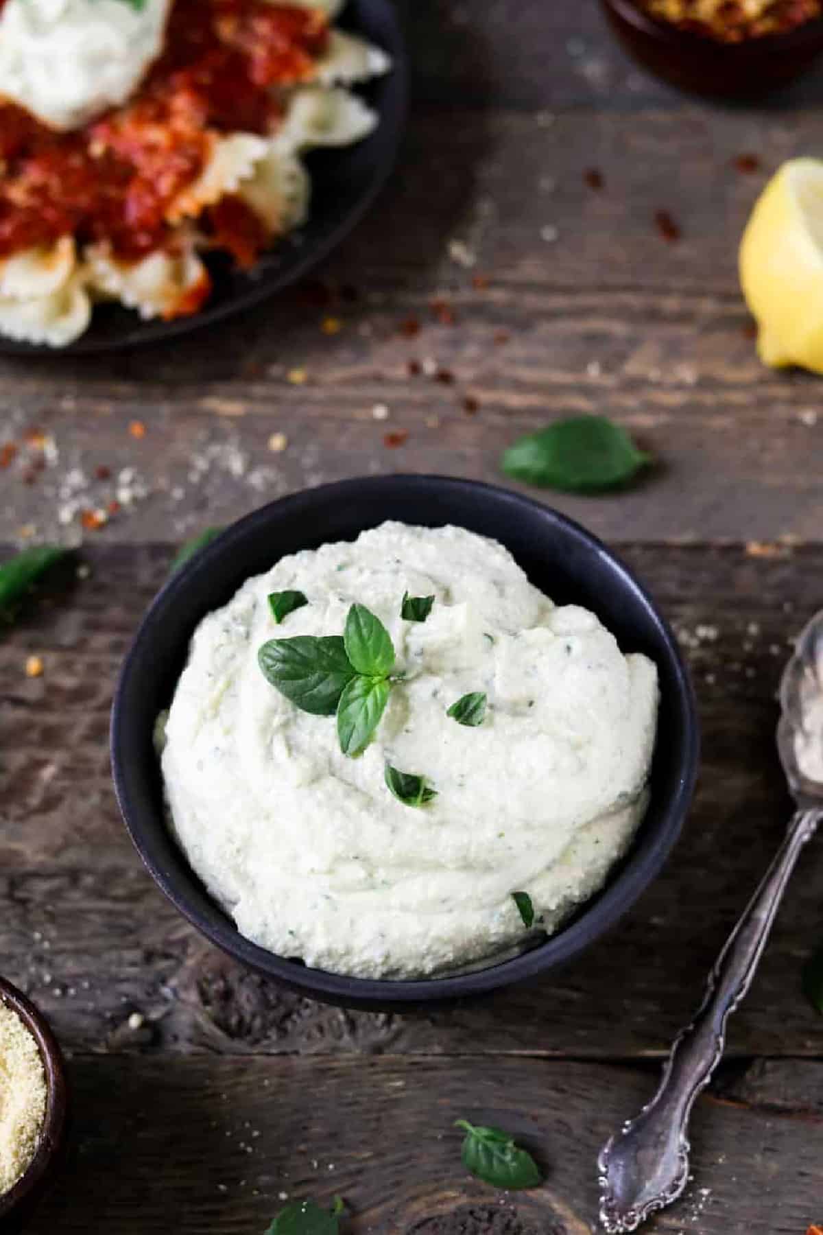 overhead view of vegan ricotta cheese in a black bowl with a spoon on the side. 