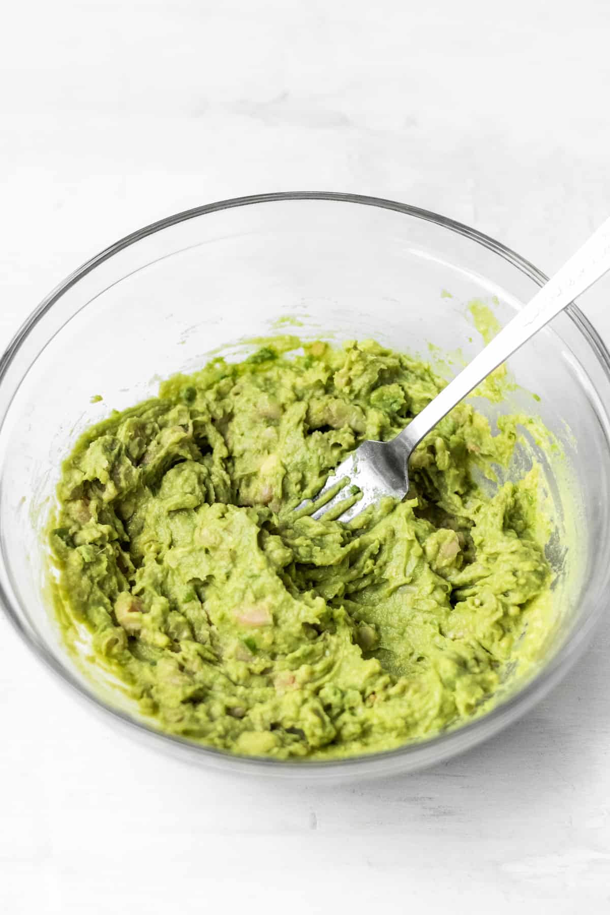 Mashing avocado and white beans in a glass bowl.