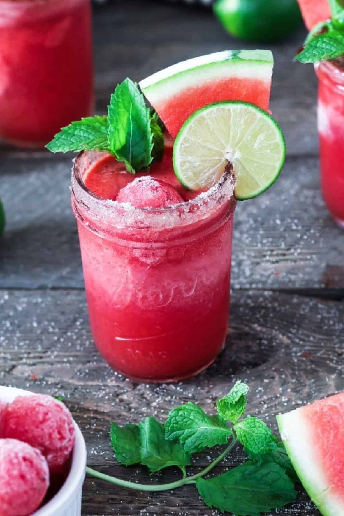 A frozen watermelon margarita in a glass garnished with lime, watermelon and mint.