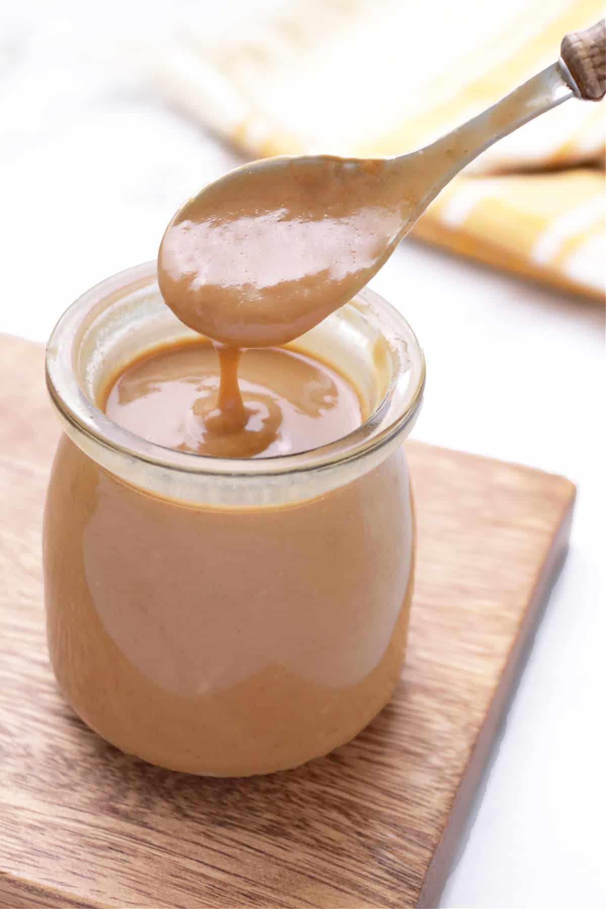 A jar of freshly made peanut sauce on a wood cutting board.