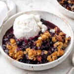 fully baked vegan blueberry crisp in a white bowl with ice cream on top.