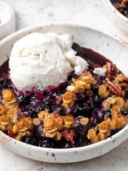 fully baked vegan blueberry crisp in a white bowl with ice cream on top.