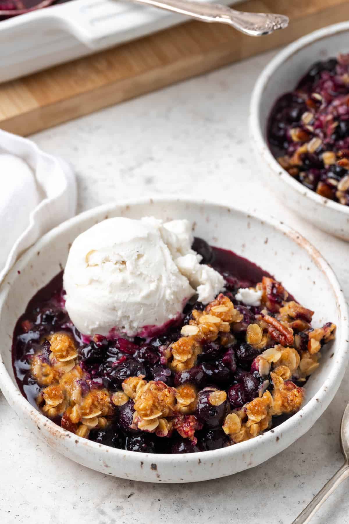 closeup view of vegan blueberry crisp in a white bowl topped with ice cream.