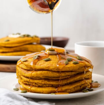 maple syrup being poured onto a stack of vegan pumpkin pancakes.
