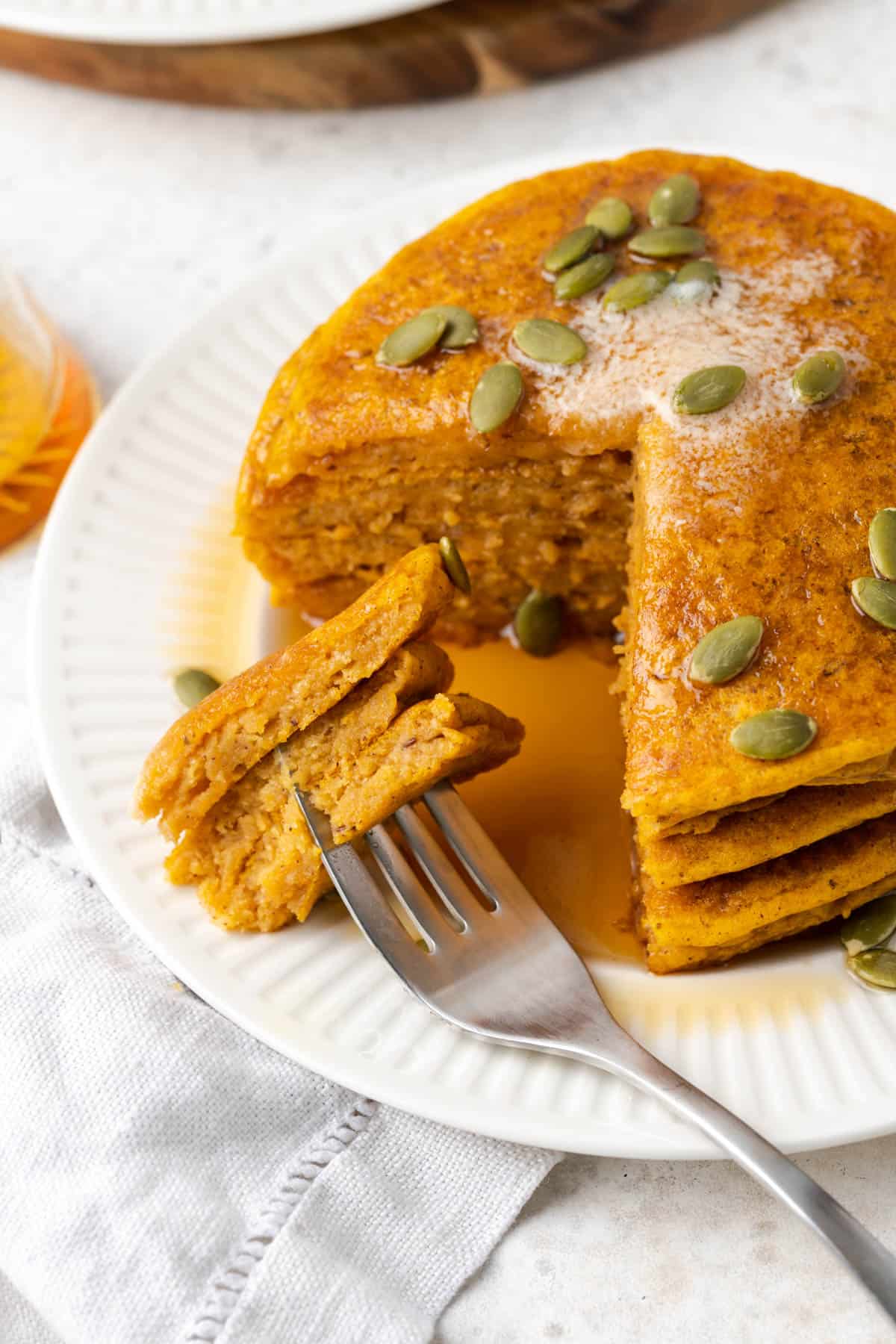 a stack of vegan pumpkin pancakes on a white plate with a fork on the side. 