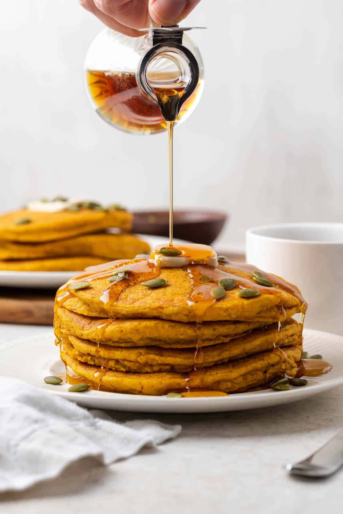 syrup being poured onto a stack of vegan pumpkin pancakes.