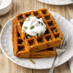 2 vegan pumpkin waffles on a white plate with a fork on the side.