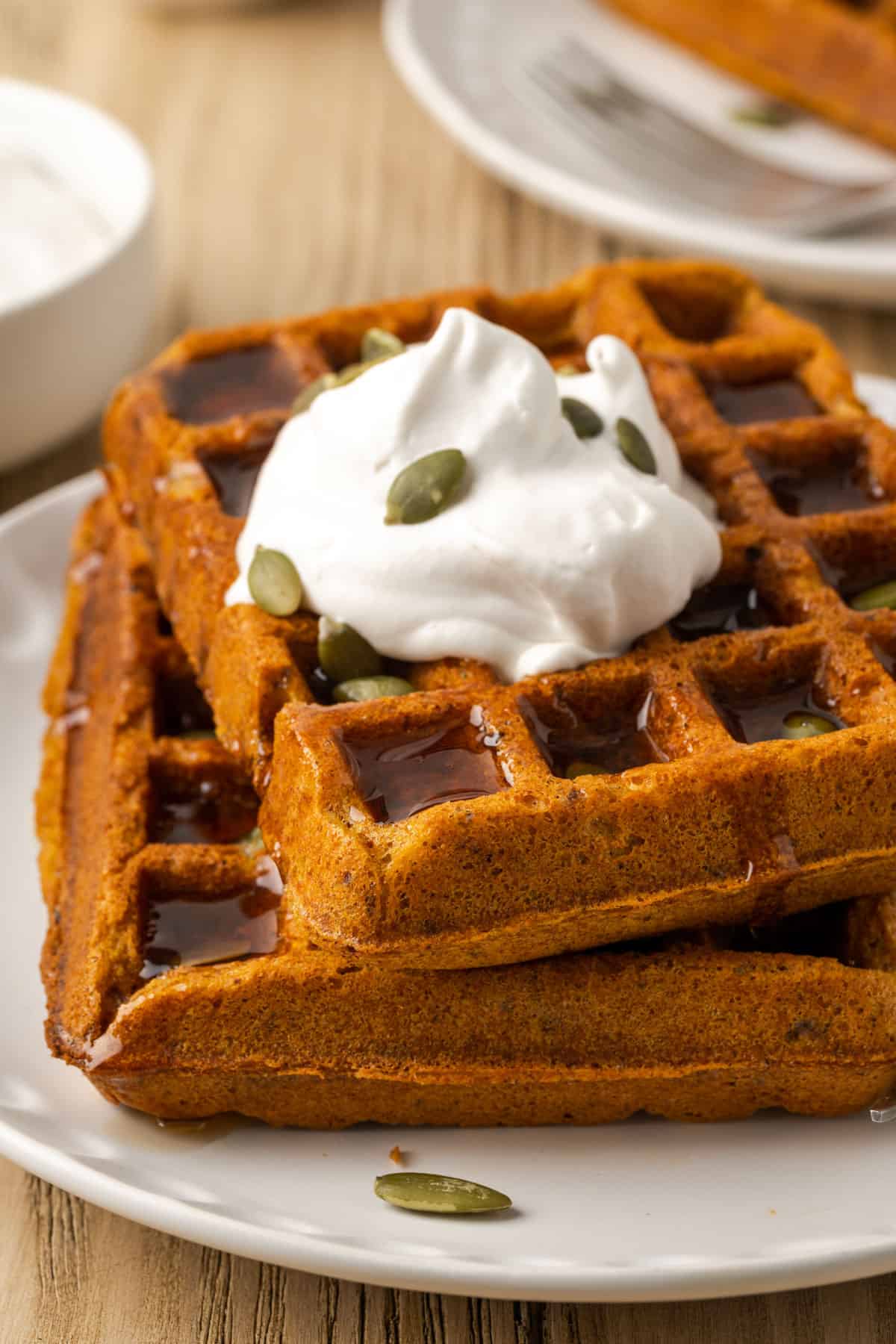 closeup view of vegan pumpkin waffles with whipped cream and syrup on top. 