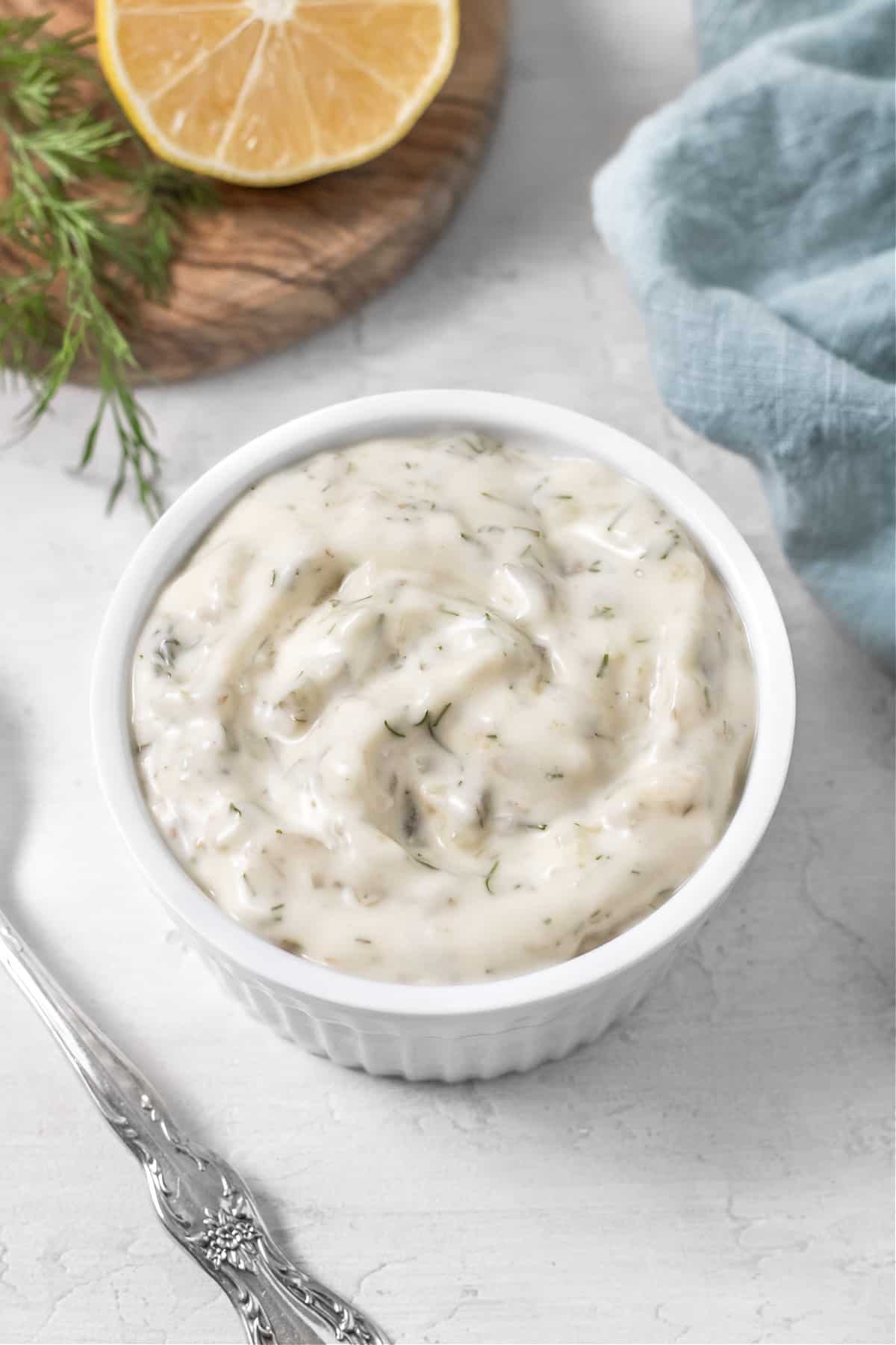 Overhead view of tartar sauce in a white ramekin with a spoon on the side. 