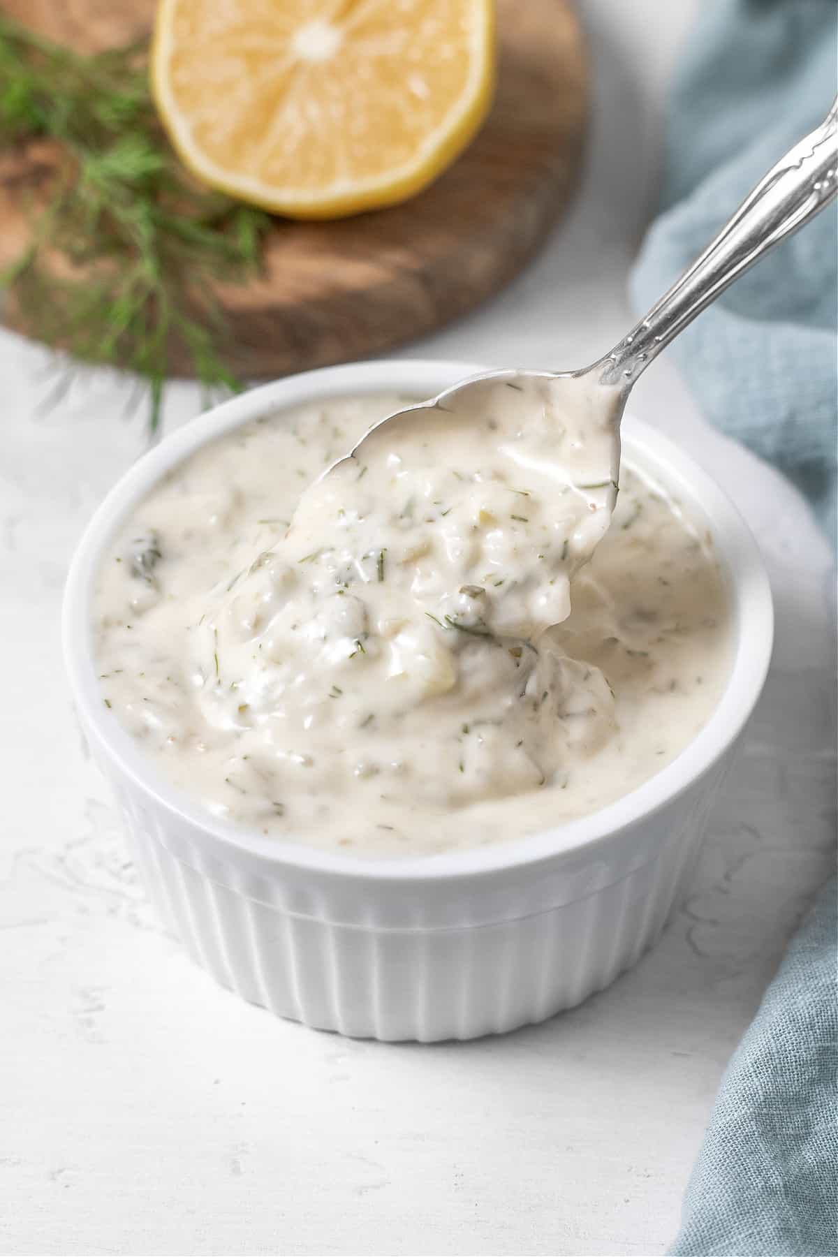 Side view of a spoon being dipped into a ramekin filled with vegan tartar sauce. 