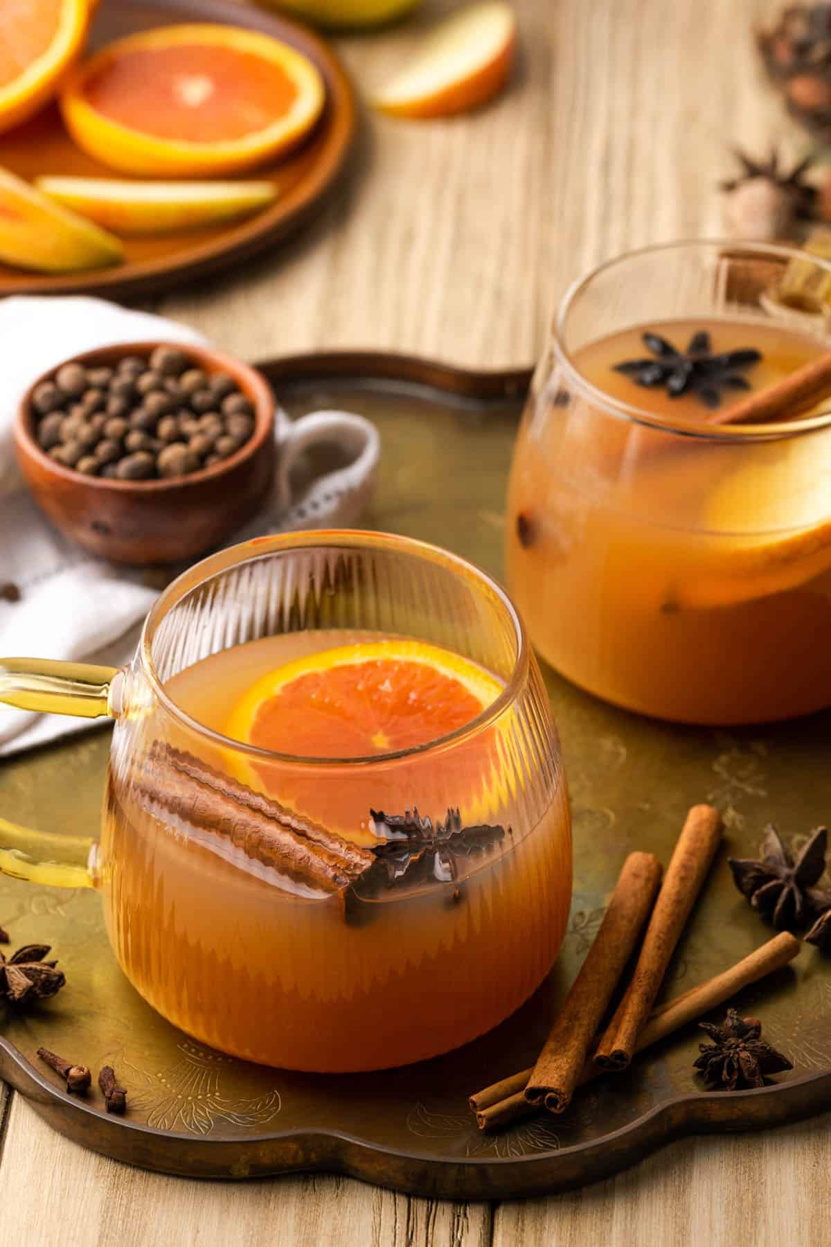 two mugs of mulled apple sider on a tarnished serving tray with spices and  fruit on the side. 