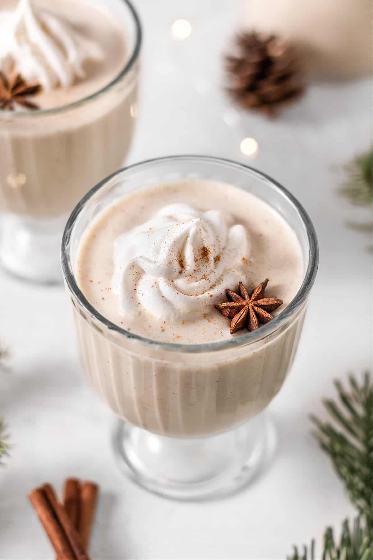 overhead view of two glasses of eggnog with whipped cream and star anise. 