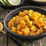 fully cooked aloo gobi in a black bowl with cilantro on top.