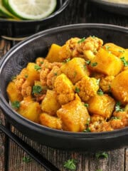 fully cooked aloo gobi in a black bowl with cilantro on top.