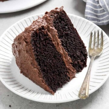 slice of chocolate cake on a white plate with a fork and napkin on the side.