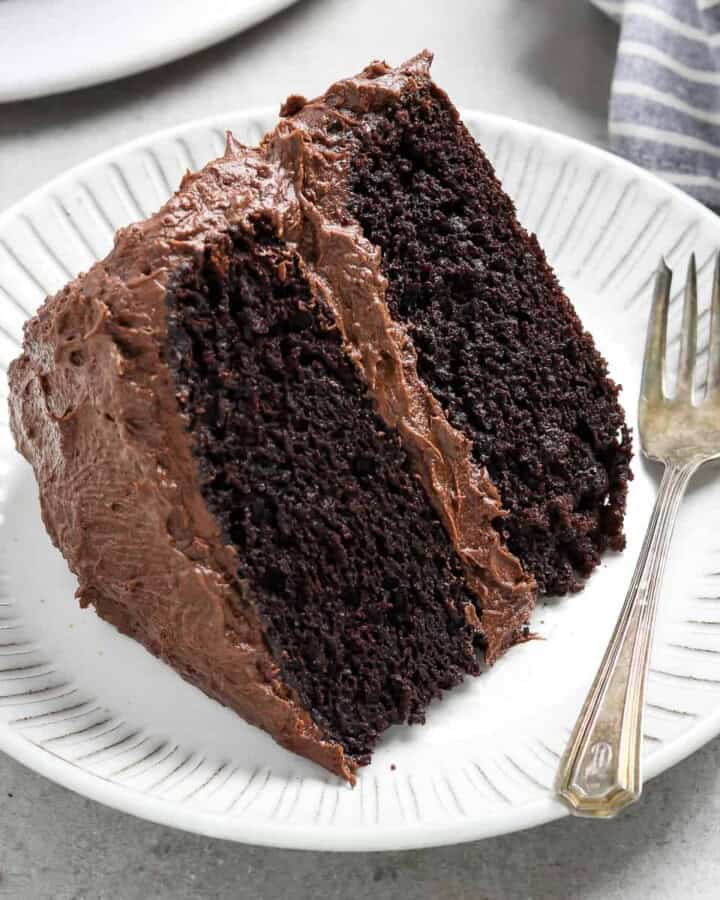 slice of chocolate cake on a white plate with a fork and napkin on the side.