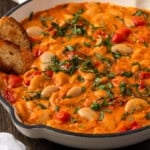 creamy tomato butter beans in a white skillet with bread inside.