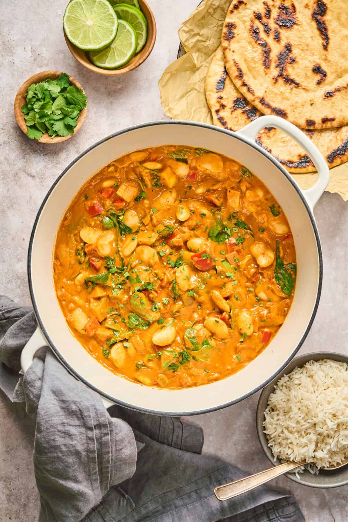 overhead view of butter bean curry in a Dutch oven with naan and rice on the side.