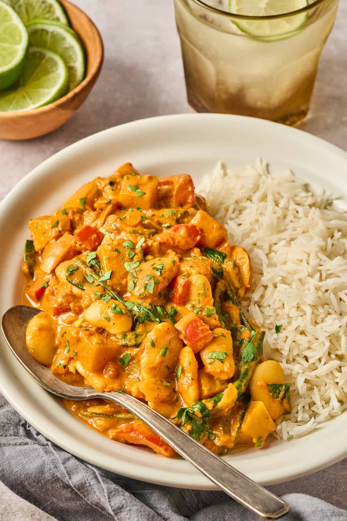 Butter bean curry and rice on a plate with a spoon on the side.