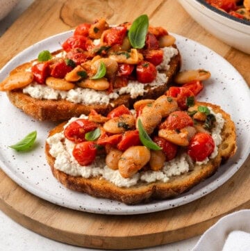 A plate of butter beans on toast slices with tomatoes and basil.