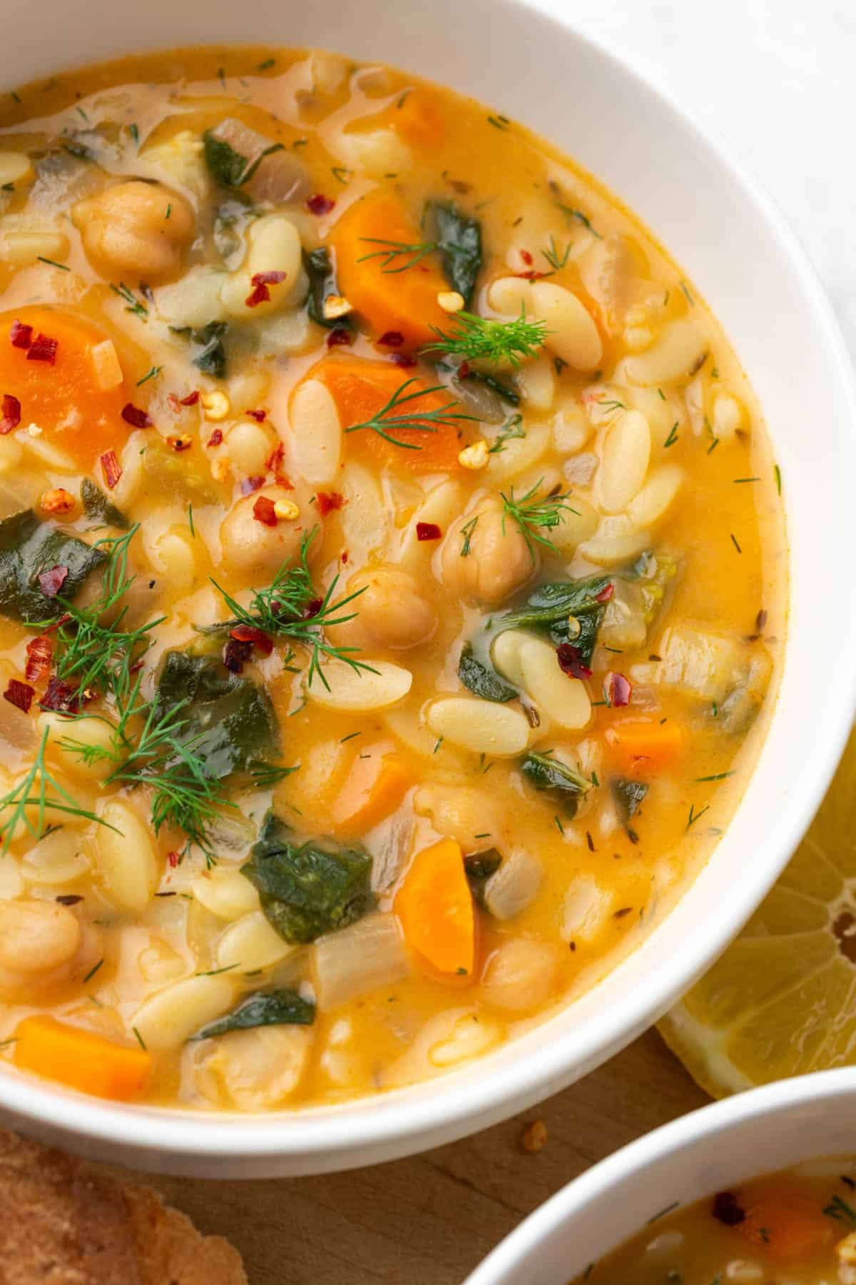 Closeup view of a bowl filled with lemon chickpea orzo soup and dill on top.
