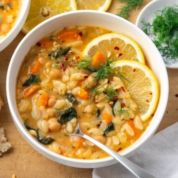 a bowl of lemon chickpea orzo soup with a spoon on the side.