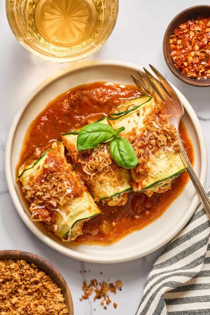 zucchini rolls on a plate with sauce and basil.