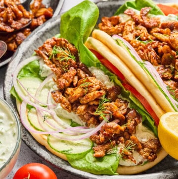 two vegan gyros on a plates with yogurt sauce in the background.