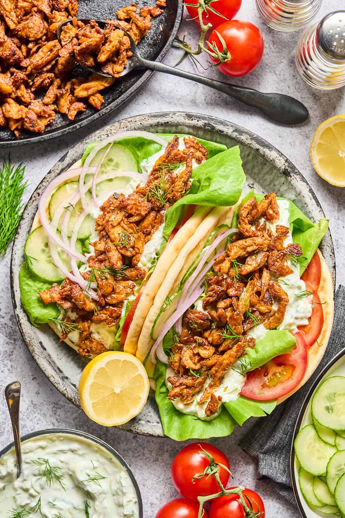 Two fully assembled vegan gyros on plate with tzatziki on the side.