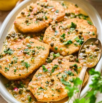 fully prepared tofu piccata on a serving plate with a spoon on the side.