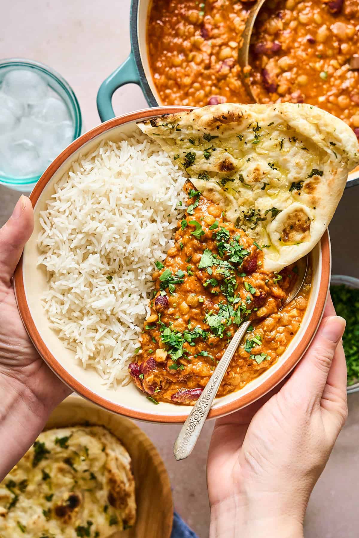 Hands holding up a bowl of prepared Vegan Dal Makhani  with rice and naan.