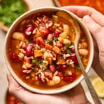 overhead view of hands holding a bowl of vegan minestrone soup.