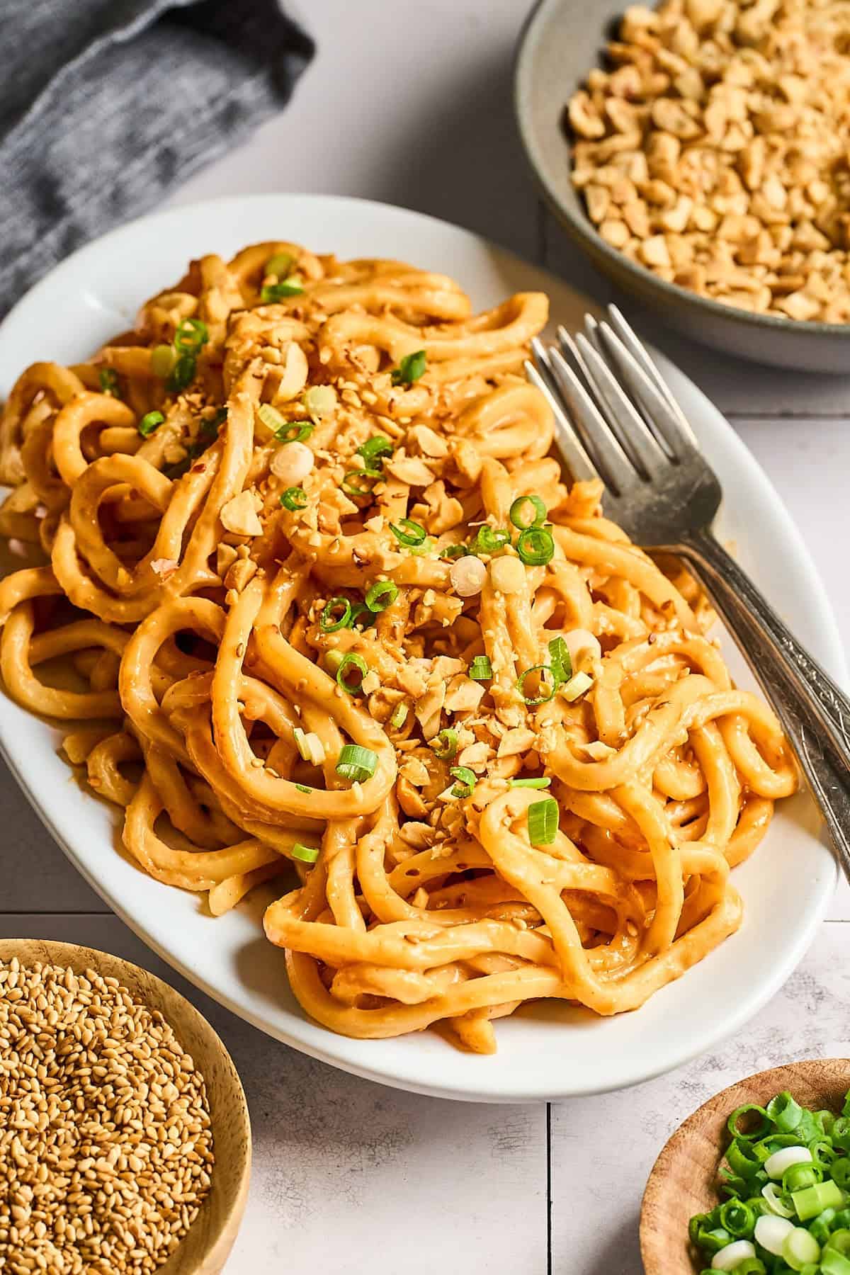 Fully cooked and garnished peanut butter noodles on a serving dish with a fork on the side. 