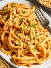 side view of peanut butter noodles on a white serving plate.