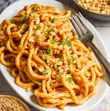 side view of peanut butter noodles on a white serving plate.