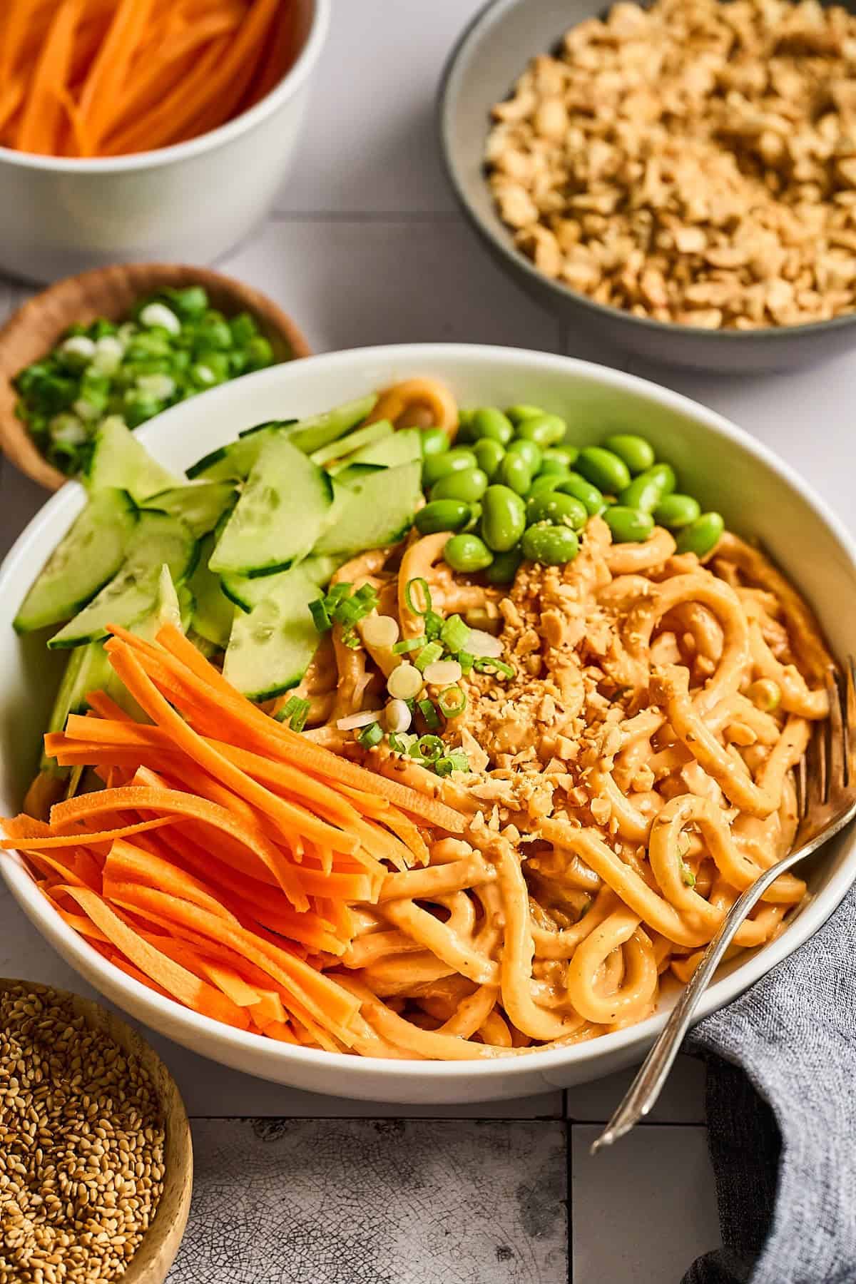 Bowl of peanut butter noodles with carrots and cucumbers on the side. 