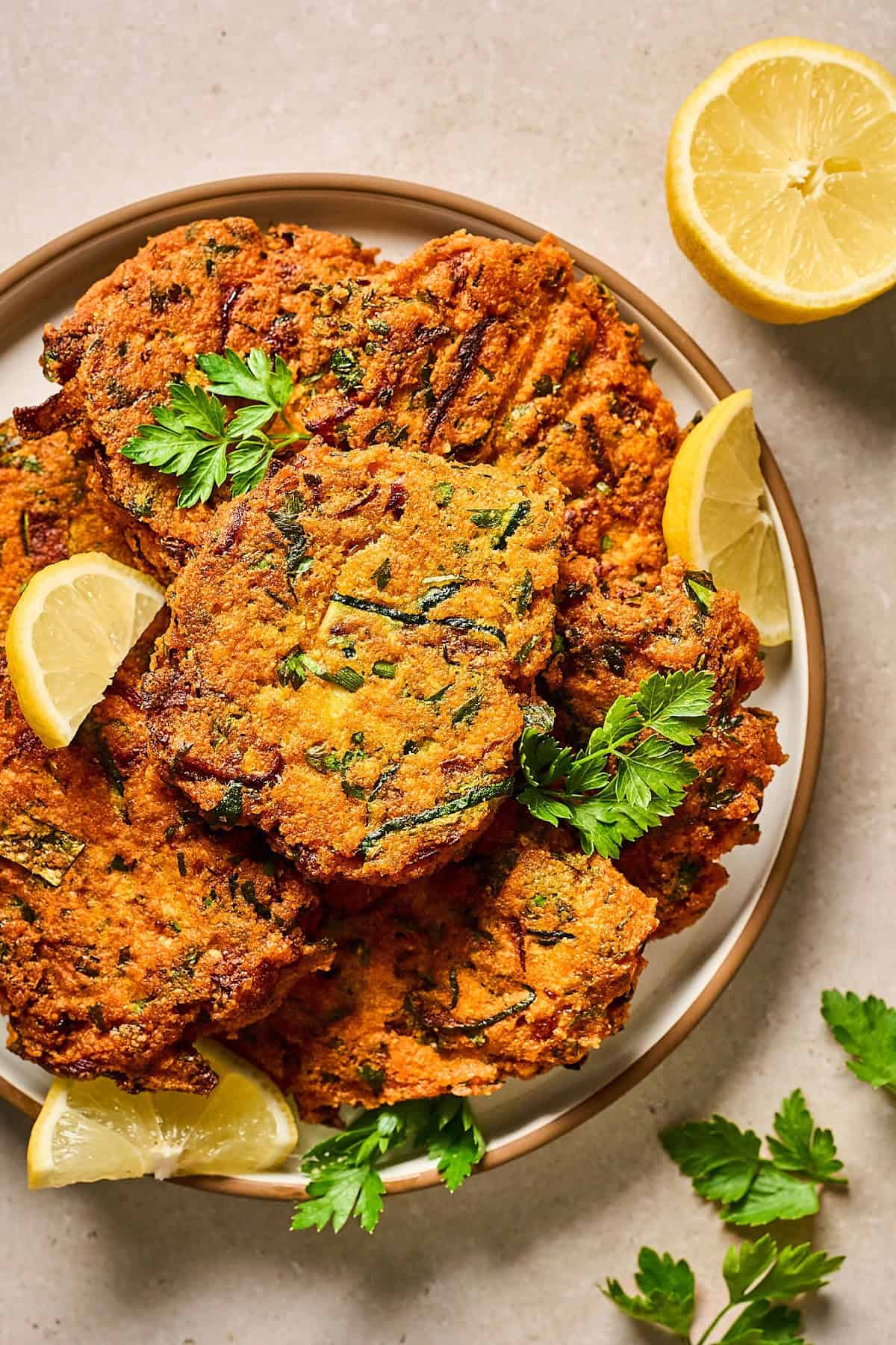 overhead view of red lentil zucchini fritters on a plate with lemon on the side.