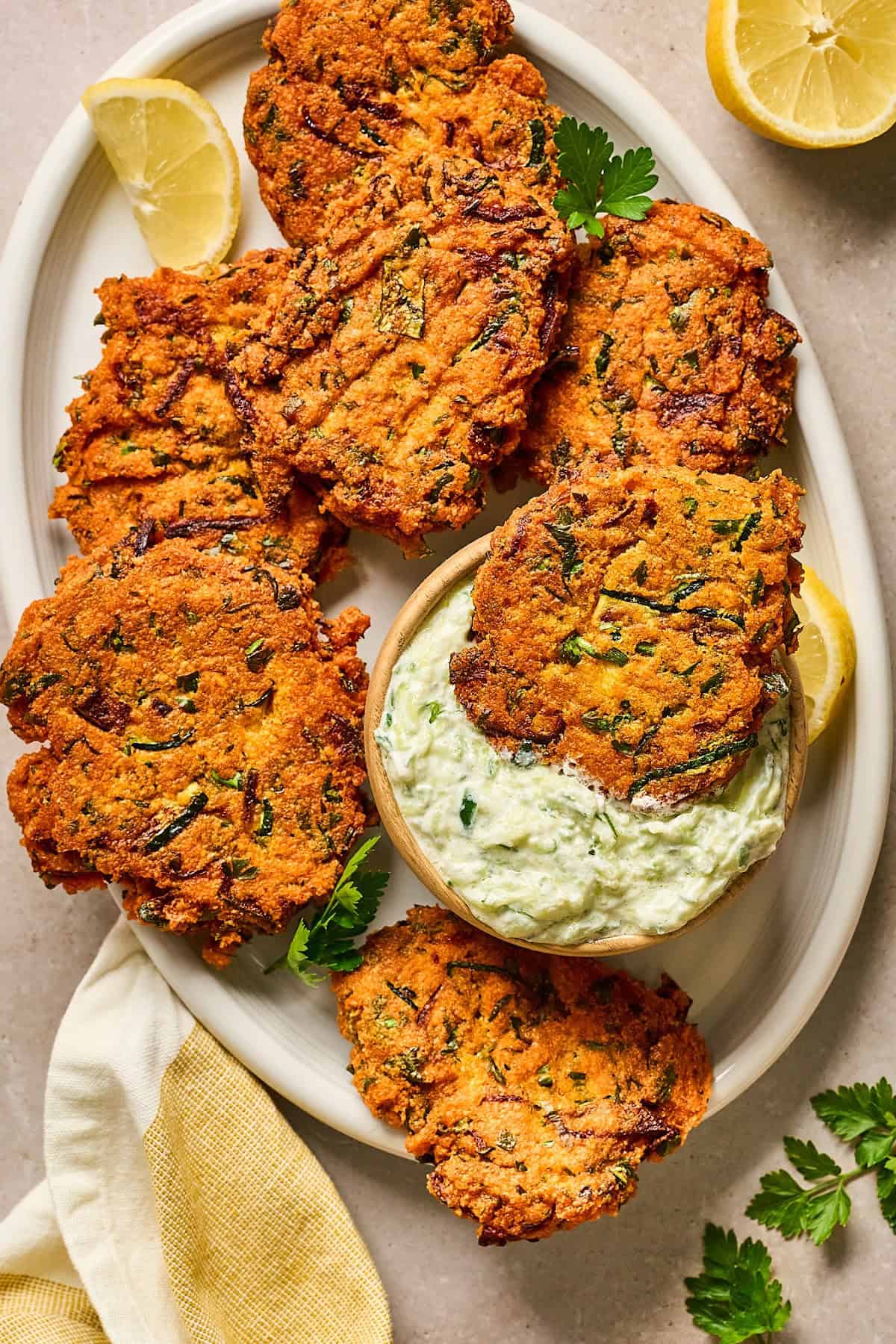 overhead view of red lentil fritters on a serving plate with dipping sauce on the side.