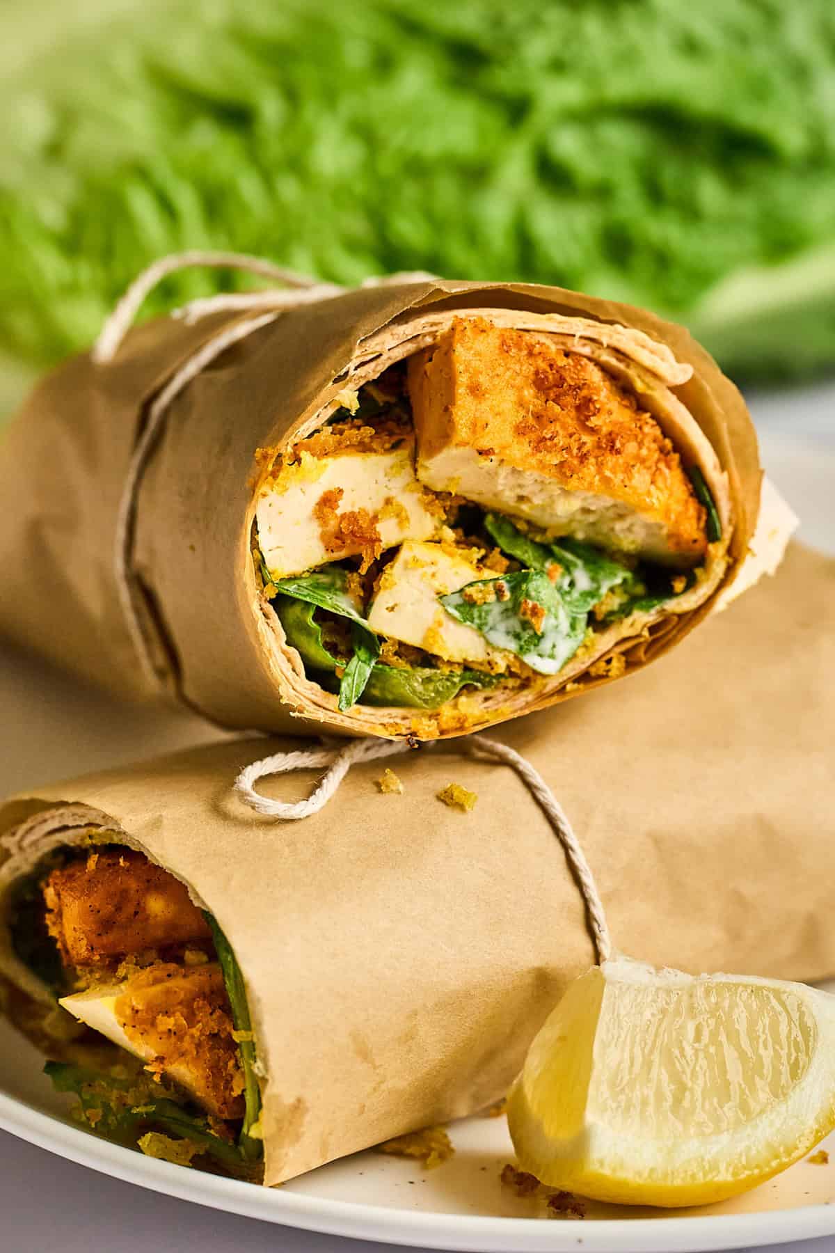 closeup view of vegan chicken caesar wrap on a white plate with a lemon wedge on the side. 
