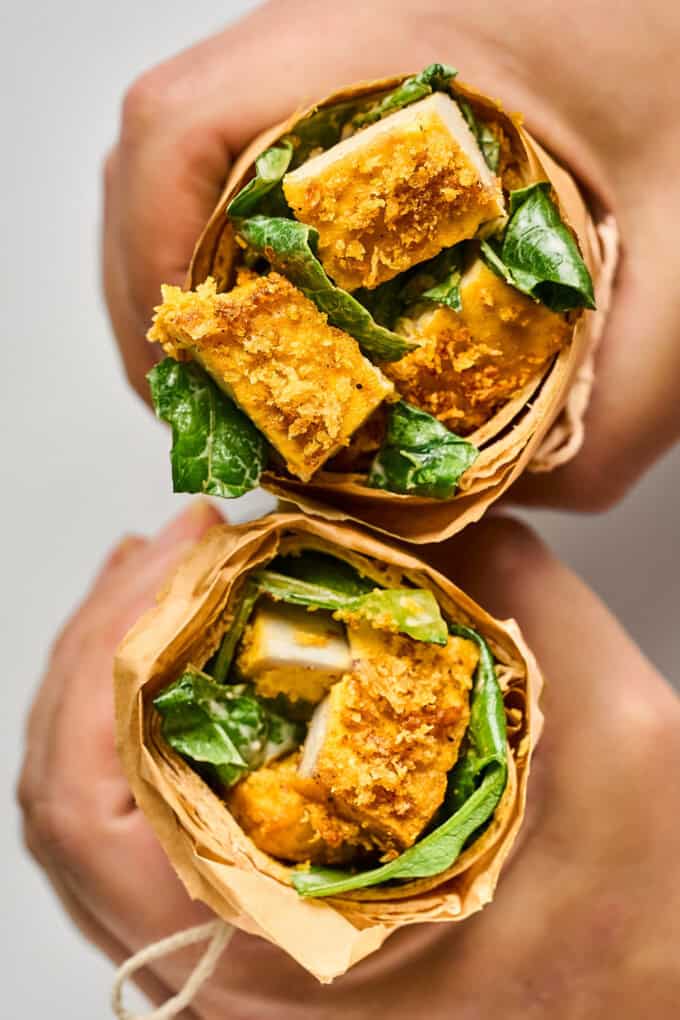 two hands holding a sandwich that is cut in half.