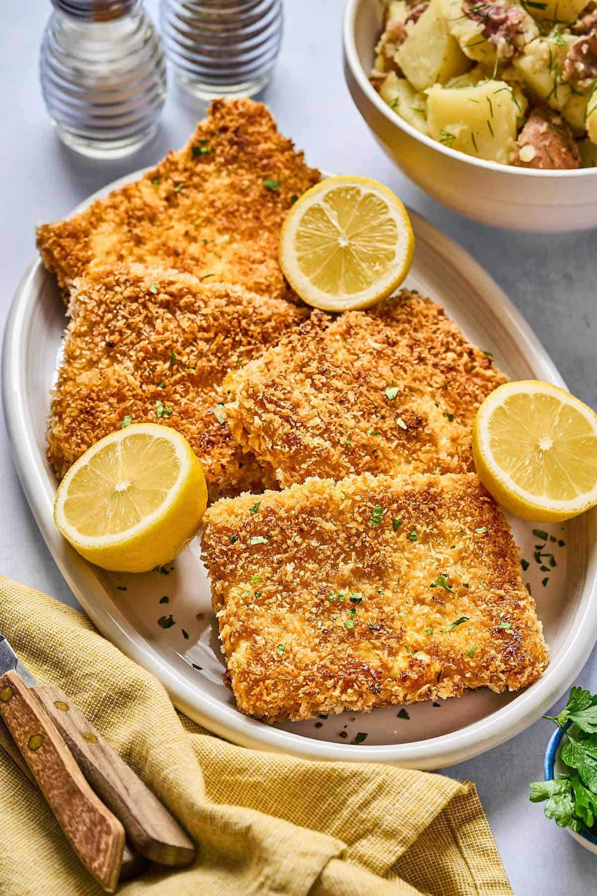 four slices of tofu schnitzel with lemon on a serving plate.